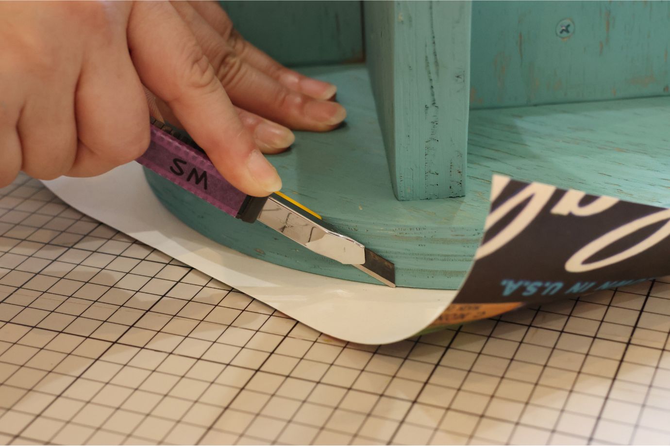 スツールを逆さまにして壁紙のはみ出ている部分をカット